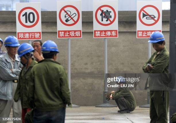 Construction worker squats as others stand by safety signs outside a real estate project in Beijing on June 16, 2009. Chinese Premier Wen Jiabao said...