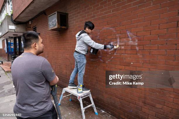 Young man cleaning graffiti off a brick wall using a gel cleaner applied with a paintbrush in Whitechapel on 25th May 2023 in London, United Kingdom....