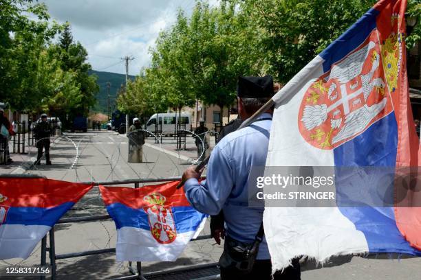 Man holding a Serbian flag looks on as he stands in front of NATO-led Kosovo Force soldiers in full riot gear standing behind a barbed wire perimeter...