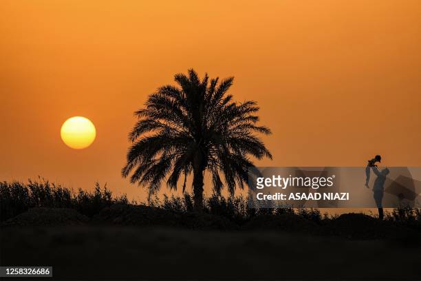 Man holds up a boy as they stand next to a palm tree at sunset on the outskirts of Iraq's southern city of Nasiriyah in Dhi Qar province on May 31,...