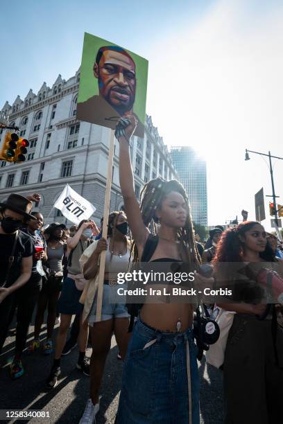 July 25: Livia Rose Johnson an organization leader of the Warriors In the Garden holds her hand up in a raised fist with the portrait of George Floyd...