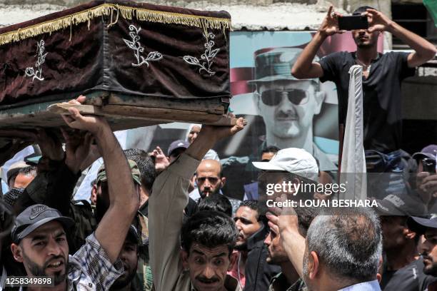 Portrait of Syria's president Bashar al-Assad looms on a wall as mourners carry the coffins of slain members of the Popular Front for the Liberation...