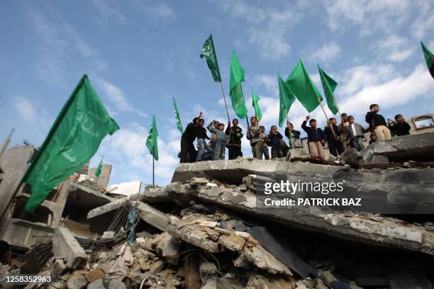 Palestinian Hamas supporters hold the movement's flag as they stand on the rubble of the building hit by an Israeli strike which killed Hamas leader...