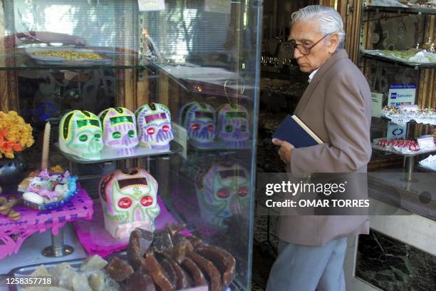 Man walks by a store front displaying candy skulls in Mexico City 31 October 2001 as part of celebrations for the Day of the Dead. Una persona...