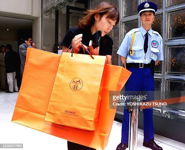 Japanese female customer carries large paper bags containing Hermes goods out from newly opened Hermes shop in central Tokyo 28 June 2001, while a...