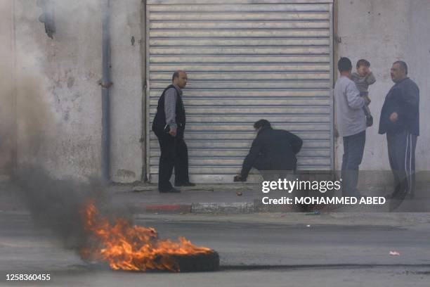 Car tire burns in the street as a Palestinian shop keeper pulls the shutter down on his store as a sign of respect following the assassination by...