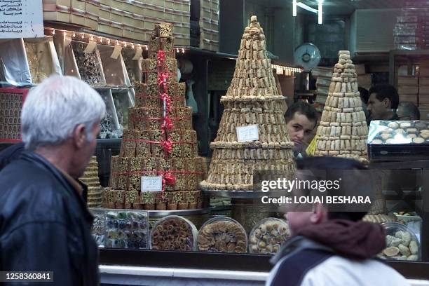 Syrians look 24 November 2003 at a sweets shop window in Damascus, especially decorated for the upcoming Eid al-Fitr holiday, which marks the end of...