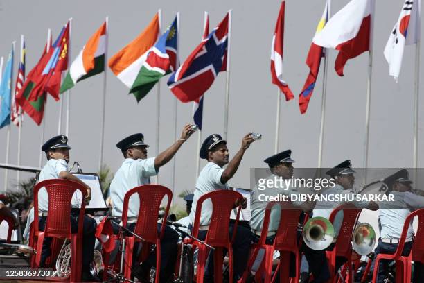 Members of the Indian Air Force Band hold up cameras as they photograph aircraft performing flight demonstrations during the inauguration of Aero...