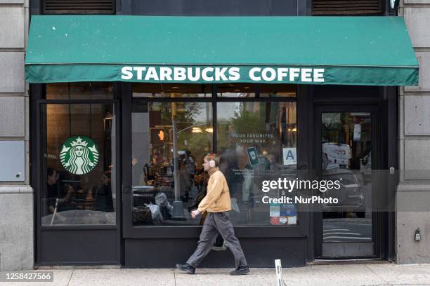 Store front of a Starbucks Coffee shop located in Broadway Avenue in Manhattan NY with people walking by and the famous logo of the twin-tailed...