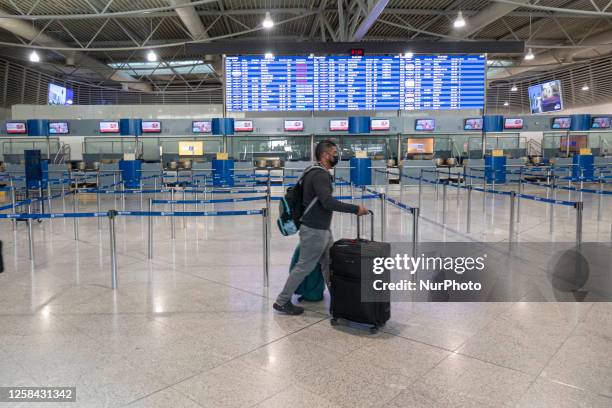 Passenger holding baggage are seen walking in front of the departure screen board and the check-in counters, pulling their luggage. People who travel...