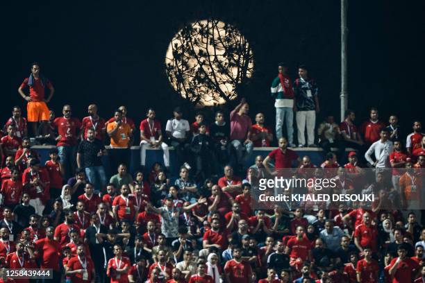 The waning gibbous moon rises behind a tree and spectators at Cairo International Stadium on June 4, 2023 during the first-leg final football match...