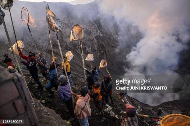 Villagers use nets to catch offerings thrown by members of the Tengger sub-ethnic group in the crater of the active Mount Bromo volcano as part of...