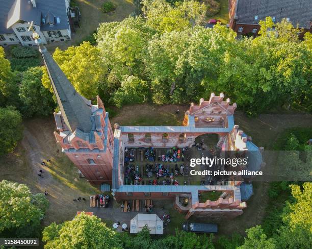 June 2023, Brandenburg, Reitwein: Visitors of a concert sit in the evening in the church of Reitwein . The church without a roof is idyllically...