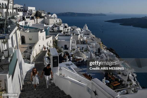 Couple walks in a street overlooking the Santorini caldera, in Fira on the island of Santorini on June 3, 2023.