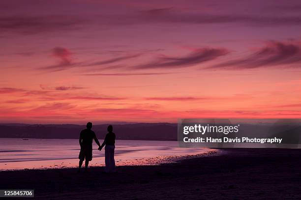 couple on beach watching sunset - marazion-cornwall-england photos et images de collection