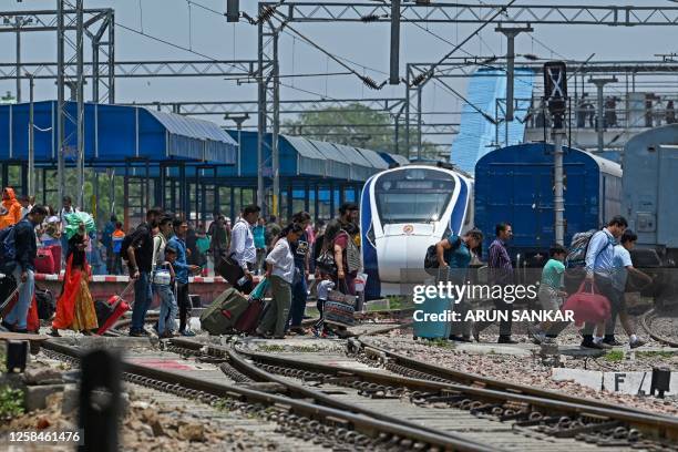 Vande Bharat Express train's passengers cross railway tracks upon their arrival at the Delhi Cantt station in New Delhi on June 5, 2023. Indian...