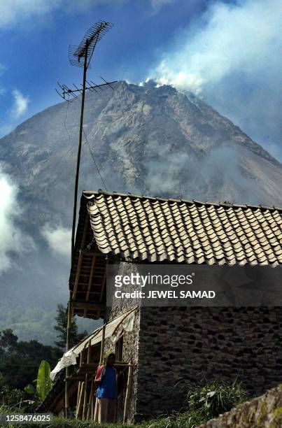 As Mount Merapi churns smokes in backdrop, a woman stands in front her house located on a slop of Mount Merapi, in Tlogolele village, Central Java,...