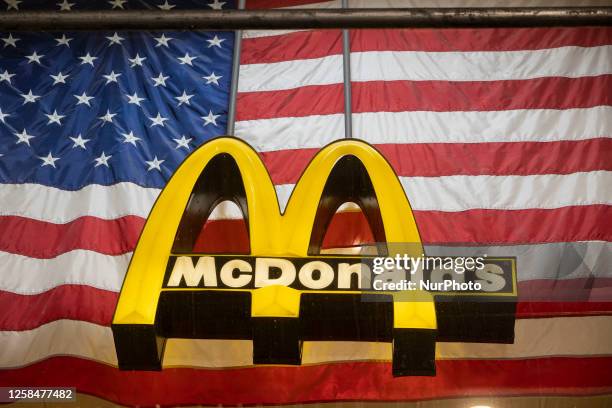 An illuminated lofo of McDonald's corporation in front of an American flag in the storefront at Broadway avenue in New York City, USA. McDonalds is a...