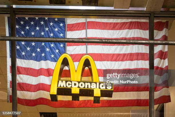 An illuminated lofo of McDonald's corporation in front of an American flag in the storefront at Broadway avenue in New York City, USA. McDonalds is a...