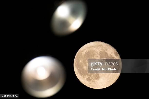 Colorful pink Strawberry moon illuminates the night sky behind street lights. Close-up of the June full moon, nicknamed as Strawberry moon as seen...