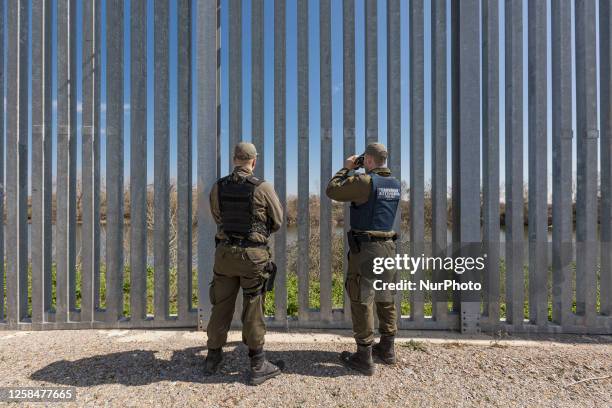 Police officer searches the area for people with binoculars. Greek border police officers patrol along the steel fence next to Evros river between...