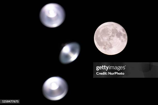 Colorful pink Strawberry moon illuminates the night sky behind street lights. Close-up of the June full moon, nicknamed as Strawberry moon as seen...