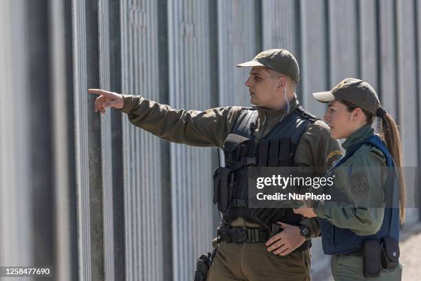 Police officer searches the area with binoculars while another officer it talking to the radio. Greek border police officers patrol along the steel...