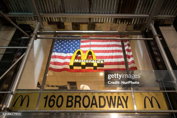 An illuminated lofo of McDonald's corporation in front of an American flag in the storefront at Broadway avenue in New York City, USA. McDonalds is a...