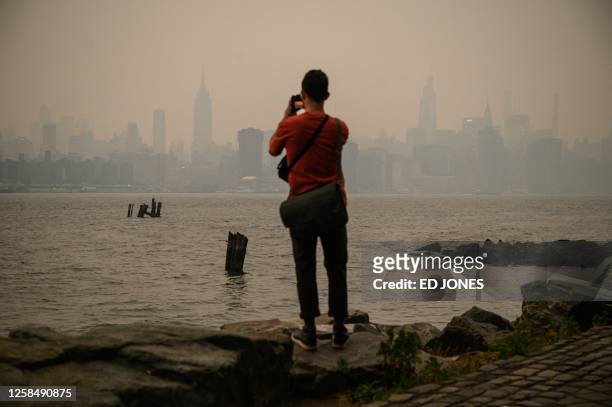 Man stands before the New York city skyline and east river shrouded in smoke, in Brooklyn on June 6, 2023. Smoke from the hundreds of wildfires...