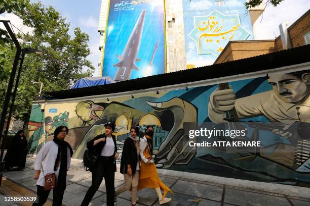 Women walk along a mural painting behind which appears a giant billboard bearing a picture of the 'Fattah' hypersonic missile, in Tehran on July 7,...
