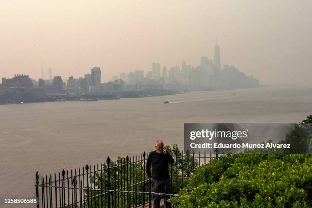 Person stands in front of the New York City skyline as its covered with haze and smoke from wildfires in Canada on June 7, 2023 in Weehawken, New...