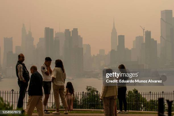 People stand in a park as the New York City skyline is covered with haze and smoke from Canada wildfires on June 7, 2023 in Weehawken, New Jersey....