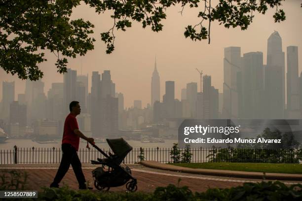 Person walks with a stroller in a park in front of the New York City skyline as it's covered with haze and smoke from Canada wildfires on June 7,...