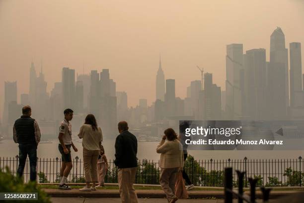 People stand in a park as the New York City skyline is covered with haze and smoke from Canada wildfires on June 7, 2023 in Weehawken, New Jersey....