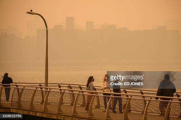 The Manhattan skyline is seen past people wearing face masks while walking along a pier as smoke from wildfires in Canada cause hazy conditions in...