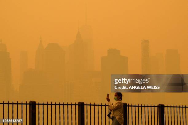 Person wearing a face mask takes photos of the skyline as smoke from wildfires in Canada cause hazy conditions in New York City on June 7, 2023. An...