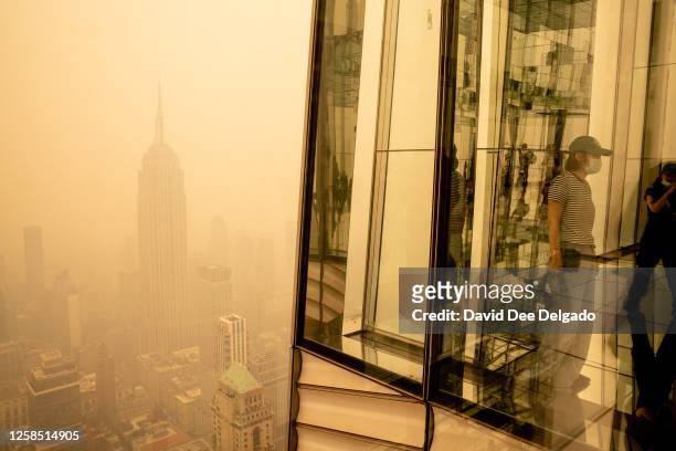 Visitors at Summit One Vanderbilt look out at a smoke-shrouded Manhattan as wildfires in Canada continue to blanket the city on June 7, 2023 in New...