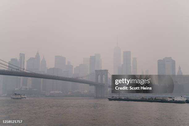 View of the Lower Manhattan skyline and Brooklyn Bridge in a dense hazy sky at sunset on June 7, 2023 in New York City. Smoke and haze from large...