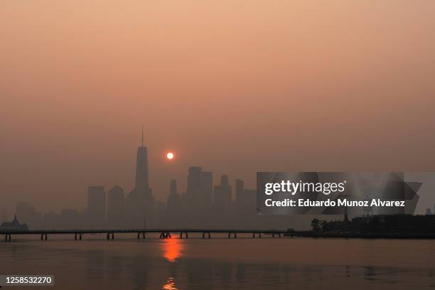 The sun rises behind The One World Trade Center and the New York skyline, while the smoke from Canada wildfires covers the Manhattan borough on June...