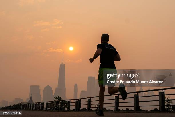 The One World Trade Center and the New York skyline is seen in the background as a man jogs through the Liberty State Park, while the smoke from...