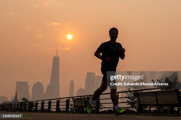 The One World Trade Center and the New York skyline is seen in the background as a man jogs through the Liberty State Park while the smoke from...