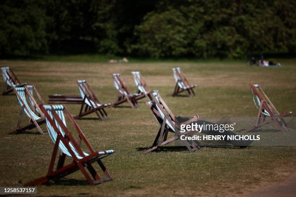 People sit on deckchairs on brown-coloured dry grass, in the sunshine in Hyde Park in central London on June 8, 2023.