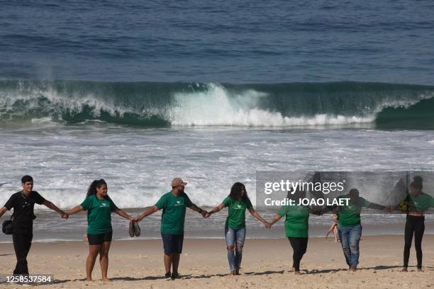 Volunteers from a Non-Governmental Organization hold hands after cleaning the Sao Conrado beach in Rio de Janeiro, Brazil on June 8, 2023 in the...