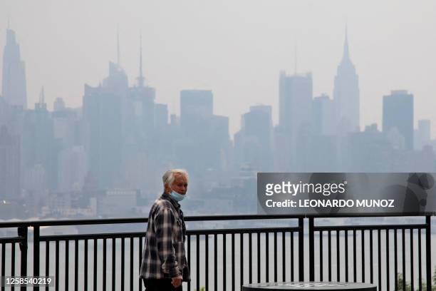 The Manhattan skyline is seen across the Hudson river past a pedestrian walking along the waterfront in West New York, New Jersey, on June 8 as smoke...