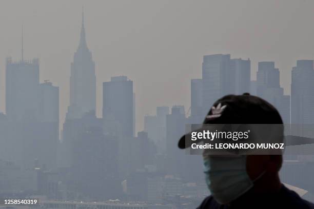 The Manhattan skyline is seen across the Hudson river as a man wearing a mask walks along the waterfront in West New York, New Jersey, on June 08 as...