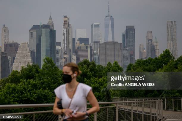 Woman wearing a face mask walks before the skyline of lower Manhattan as smoke from wildfires in Canada cause hazy conditions in New York City on...