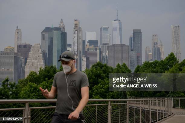 Person wearing a face mask walks before the skyline of lower Manhattan as smoke from wildfires in Canada cause hazy conditions in New York City on...