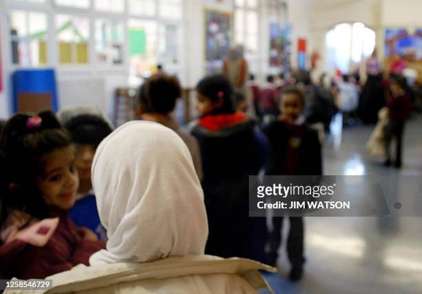 Young girl wearing a muslim headscarf stands in line talking with other girls before going out for recess play time at Featherstone Primary school 09...