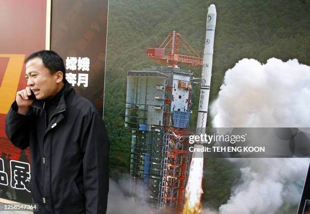 Man talks on a mobile phone next to a billboard showing Chinese made Chang'e I, the country's first lunar orbiter, blasting off from the Xichang...