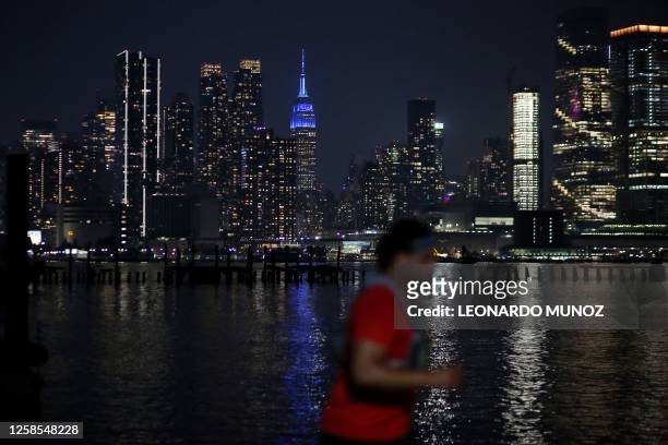 Pedestrian walks along the skyline of midtown Manhattan, New York, as seen from across the Hudson river in Weehawken, New Jersey, on June 8, 2023....